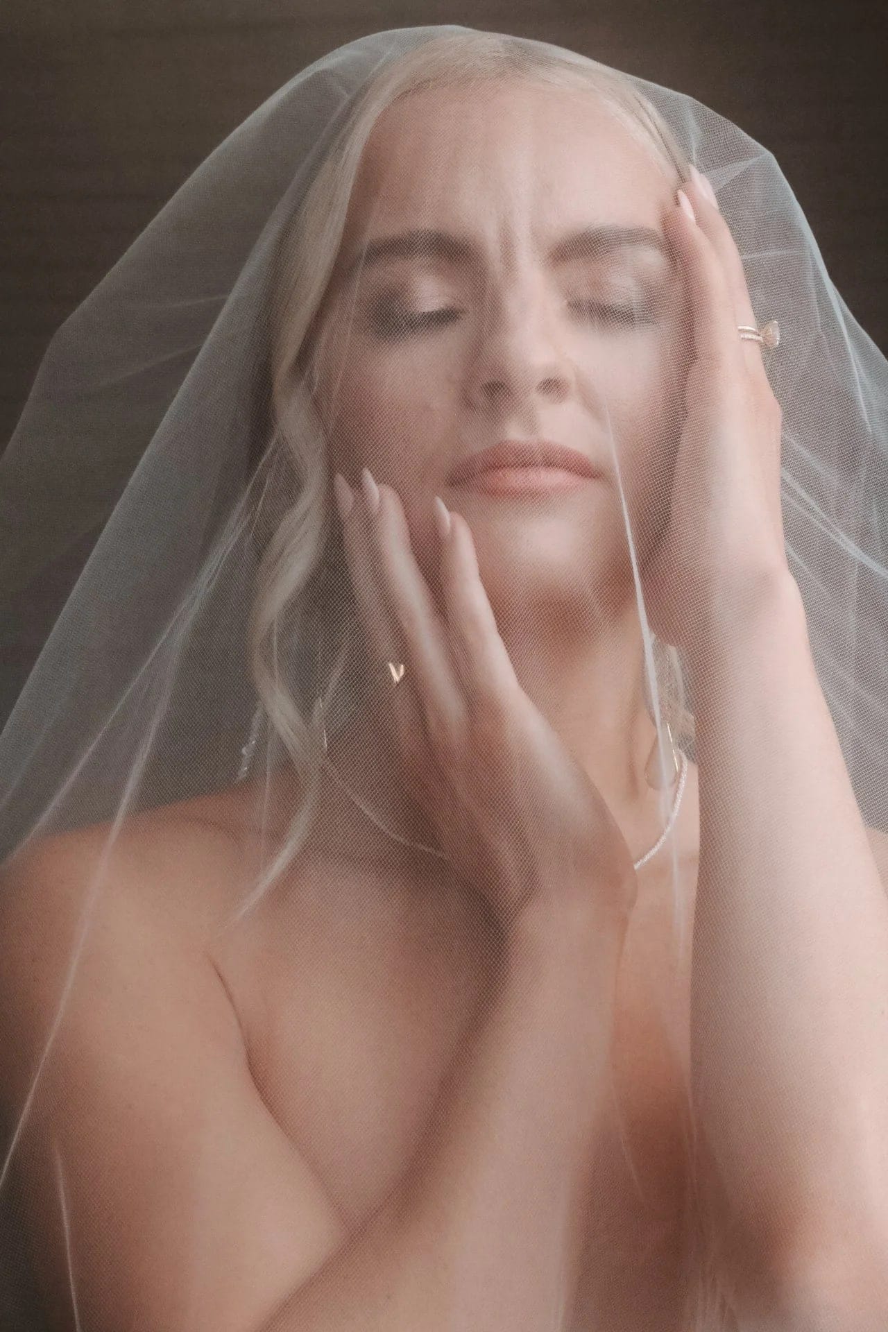 Bride beneath a sheer veil, hands framing her face