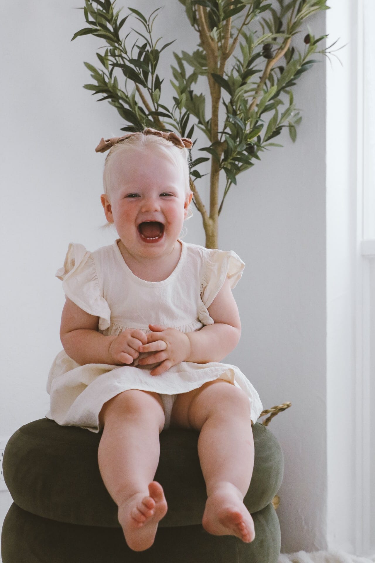 Laughing baby girl in a cream dress sitting on a green pouf